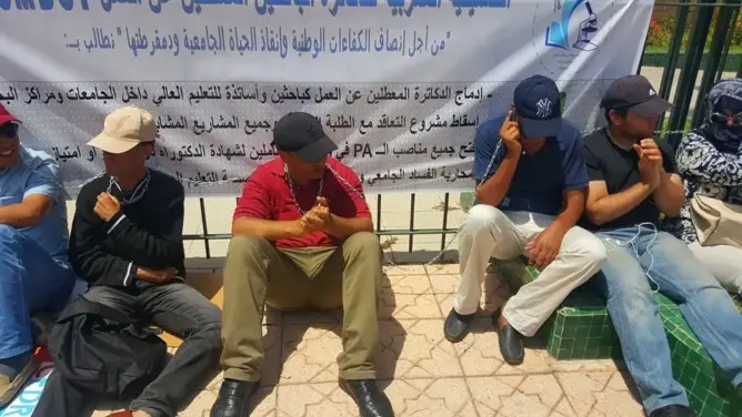 دكاترة معطلين يربطون أعناقهم بسلاسل حديدية أمام وزارة حصاد (صور)