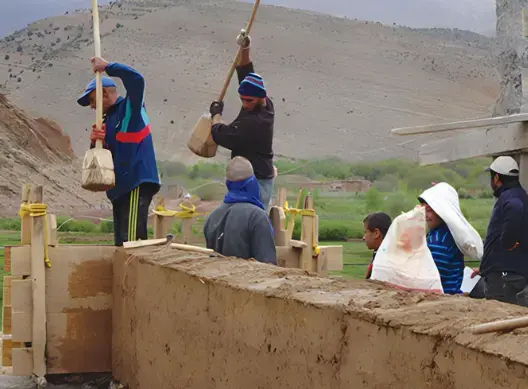 رجال يبنون جداراً تقليدياً من الطين المضغوط (البناء بالتابوت) في منطقة جبلية