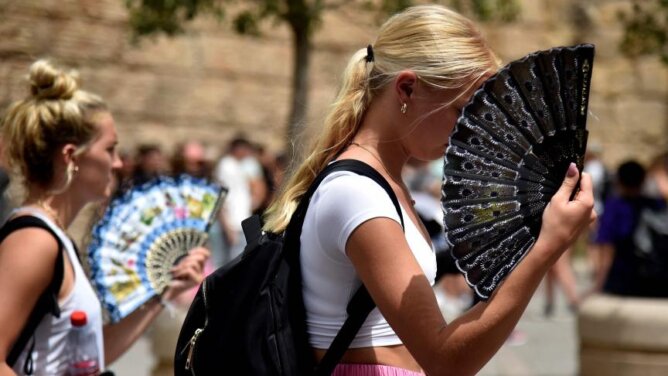 امرأة تحمل مروحة سوداء في ساحة عامة خلال موجة حر وجفاف شديدين