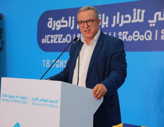 محمد أوجار خلف منبر أبيض في لقاء حزبي بخلفية زرقاء ونصوص عربية