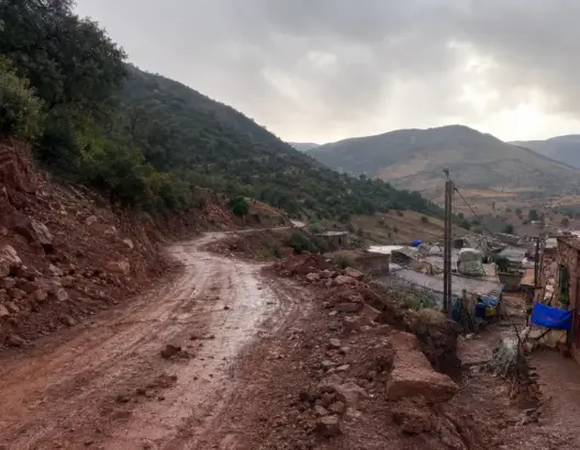 قرية جبلية صغيرة بطريق ترابي متضرر وجبال خضراء في وادي ضيق