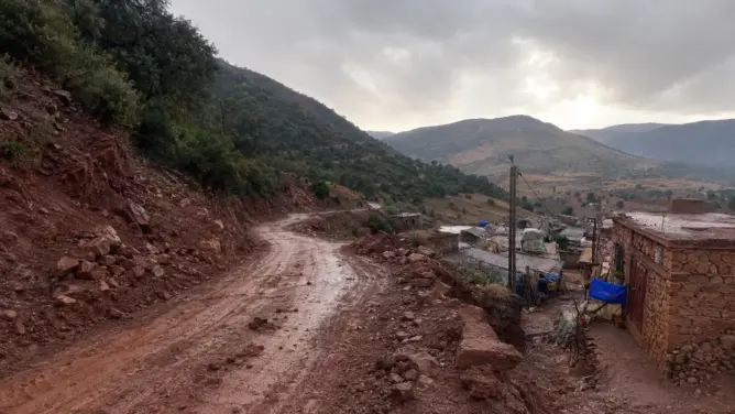 قرية جبلية صغيرة بطريق ترابي متضرر وجبال خضراء في وادي ضيق