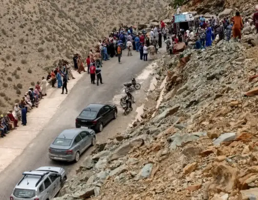 طريق جبلي ضيق محاط بالصخور وجماهير على الجانبين بعد حادث انقلاب شاحنة