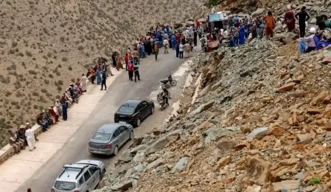 طريق جبلي ضيق محاط بالصخور وجماهير على الجانبين بعد حادث انقلاب شاحنة