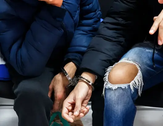 يدان مقيدتان بأغلال معدنية لشخصين أحدهما ببنطال مزقق والآخر بسترة زرقاء داكنة