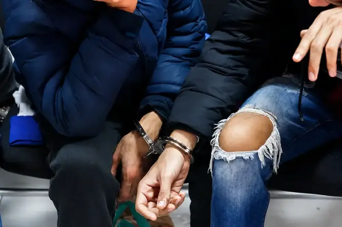 يدان مقيدتان بأغلال معدنية لشخصين أحدهما ببنطال مزقق والآخر بسترة زرقاء داكنة