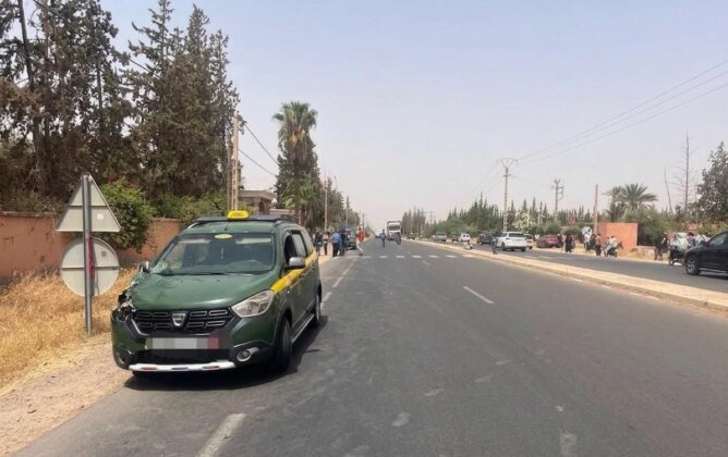 طريق حضري واسع مع سيارة أجرة خضراء وسوداء وأشجار نخيل في مراكش