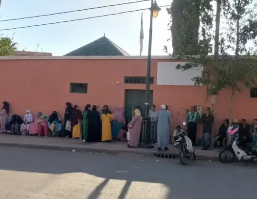 مجموعة أشخاص أمام جدار طوب أحمر في أغمات قرب مركز صحي