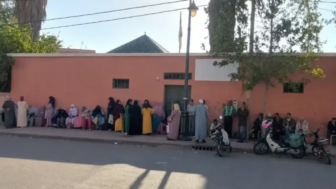 مجموعة أشخاص أمام جدار طوب أحمر في أغمات قرب مركز صحي