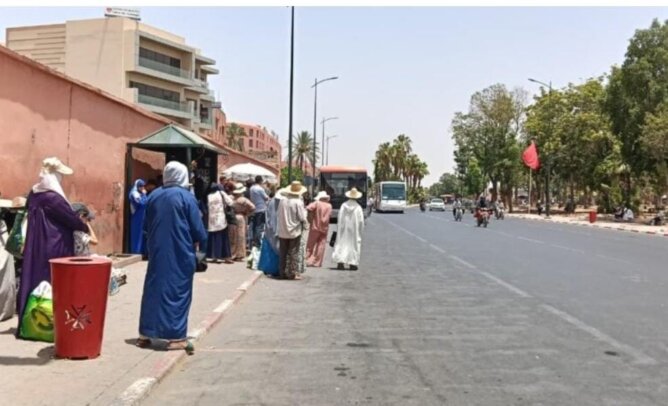 مجموعة أشخاص ينتظرون حافلة في شارع بمراكش تحت أشعة الشمس دون مظلات
