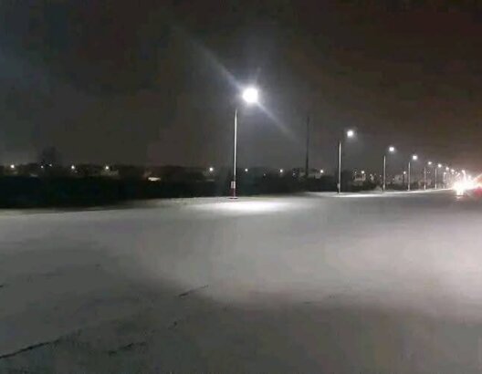 طريق ليلي مظلم بإضاءة جزئية من أعمدة الإنارة وأرض مبللة بضواحي مراكش