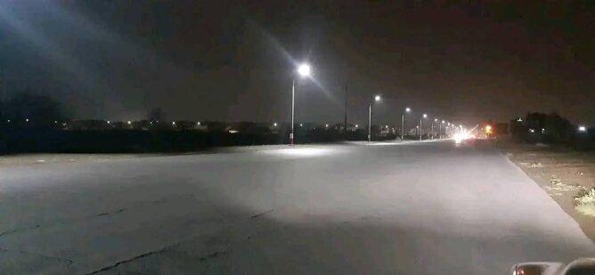 طريق ليلي مظلم بإضاءة جزئية من أعمدة الإنارة وأرض مبللة بضواحي مراكش