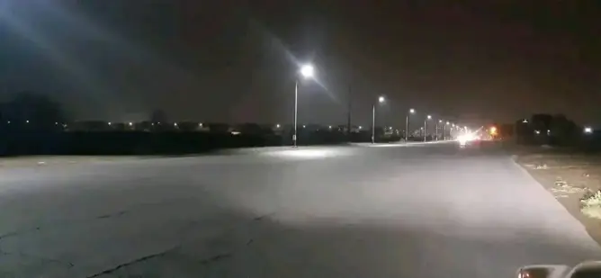 طريق ليلي مظلم بإضاءة جزئية من أعمدة الإنارة وأرض مبللة بضواحي مراكش