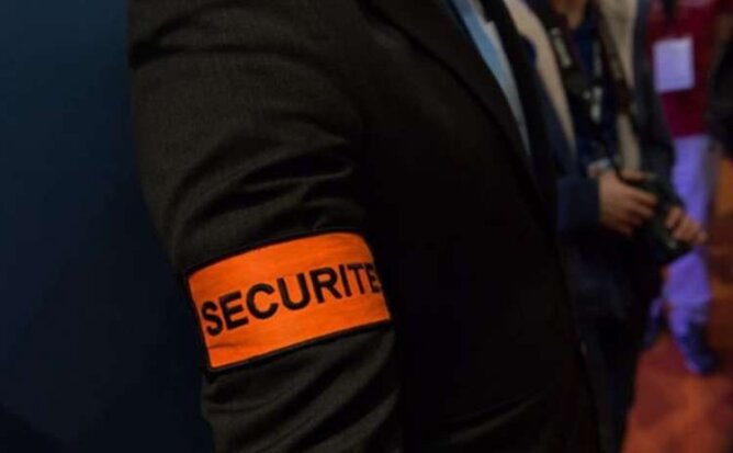 شريط أمن برتقالي مكتوب عليه SECURITE على ذراع شخص بخلفية غير واضحة