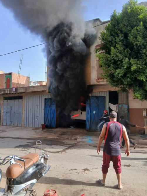 حريق ينبعث منه دخان كثيف من مبنى وساكن يرش الماء لإطفائه