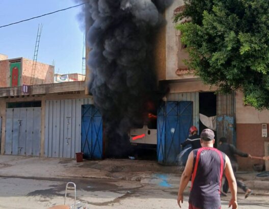 حريق ينبعث منه دخان كثيف من مبنى وساكن يرش الماء لإطفائه