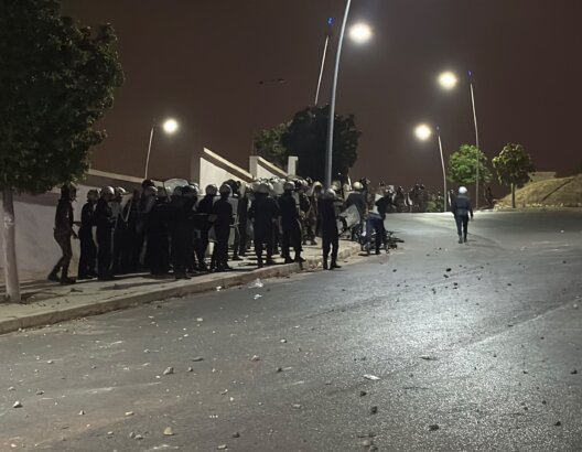 عناصر أمنية بملابس واقية ودروع في طريق ليلي مضاء وسط حجارة مبعثرة قرب الشريط الحدودي