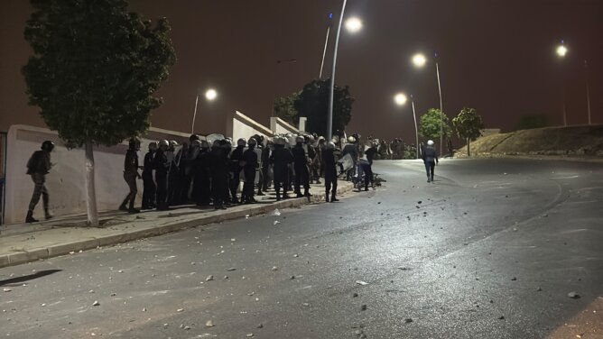 عناصر أمنية بملابس واقية ودروع في طريق ليلي مضاء وسط حجارة مبعثرة قرب الشريط الحدودي