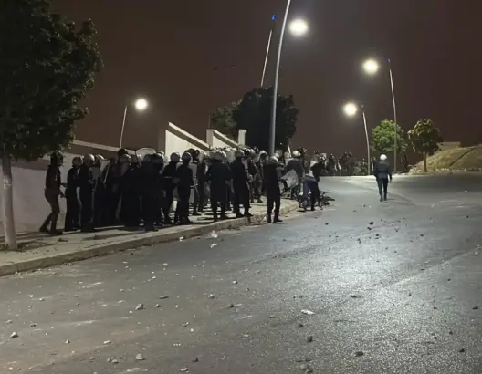 عناصر أمنية بملابس واقية ودروع في طريق ليلي مضاء وسط حجارة مبعثرة قرب الشريط الحدودي