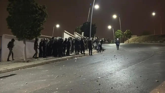 عناصر أمنية بملابس واقية ودروع في طريق ليلي مضاء وسط حجارة مبعثرة قرب الشريط الحدودي