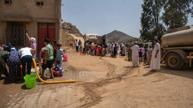 طابور طويل من الناس يحملون أوعية لملء الماء من صهاريج في منطقة ترابية بإقليم خنيفرة