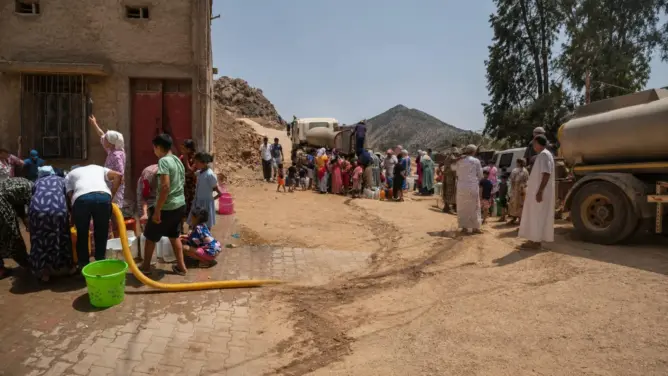 طابور طويل من الناس يحملون أوعية لملء الماء من صهاريج في منطقة ترابية بإقليم خنيفرة