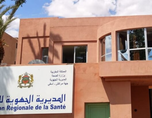 مبنى المديرية الجهوية للصحة باللافتة الرسمية وعلم أحمر وأشجار نخيل