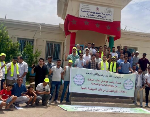 مجموعة من المحتجين أمام مبنى حكومي يحملون لافتة بالعربية وعلم المغرب