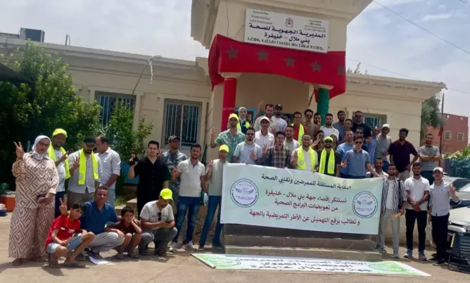 مجموعة من المحتجين أمام مبنى حكومي يحملون لافتة بالعربية وعلم المغرب